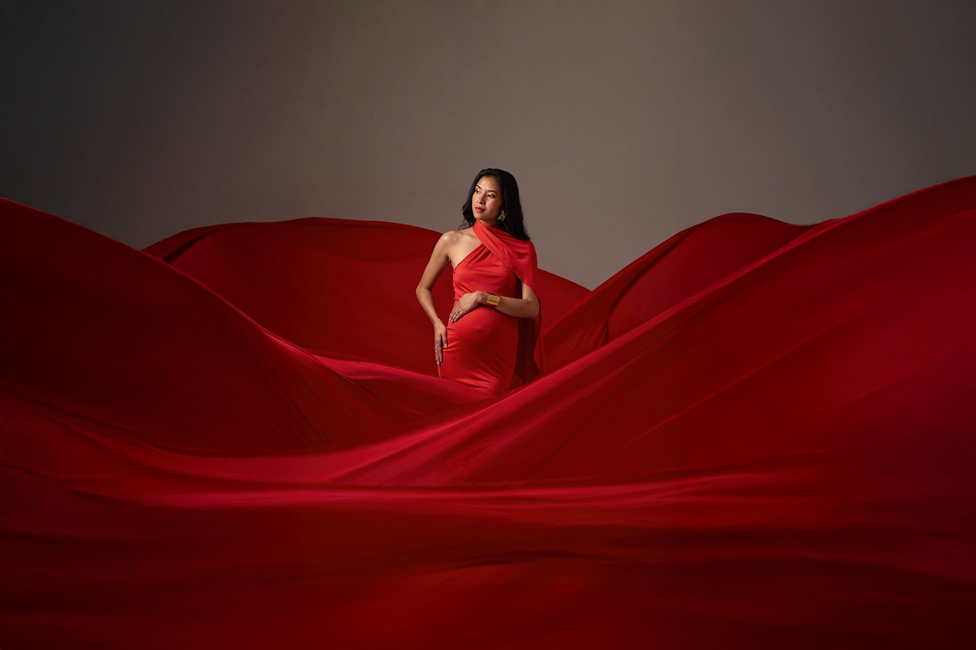Une femme enceinte en robe rouge, au milieu de vastes drapés rouges qui ondulent comme des dunes.